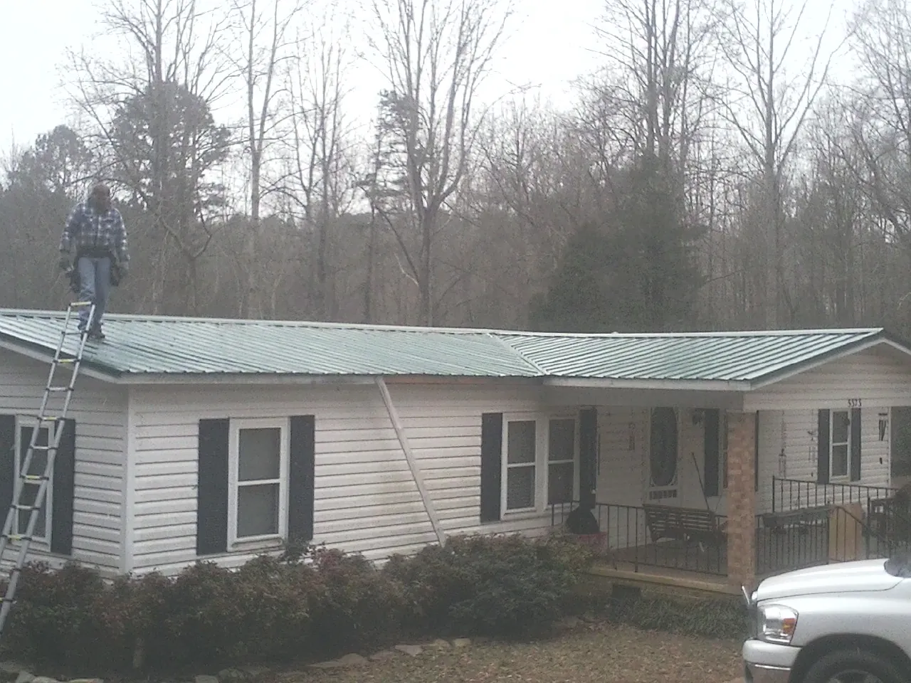 Worker on a ladder beside a new green metal roof on a ranch home in Litchfield
