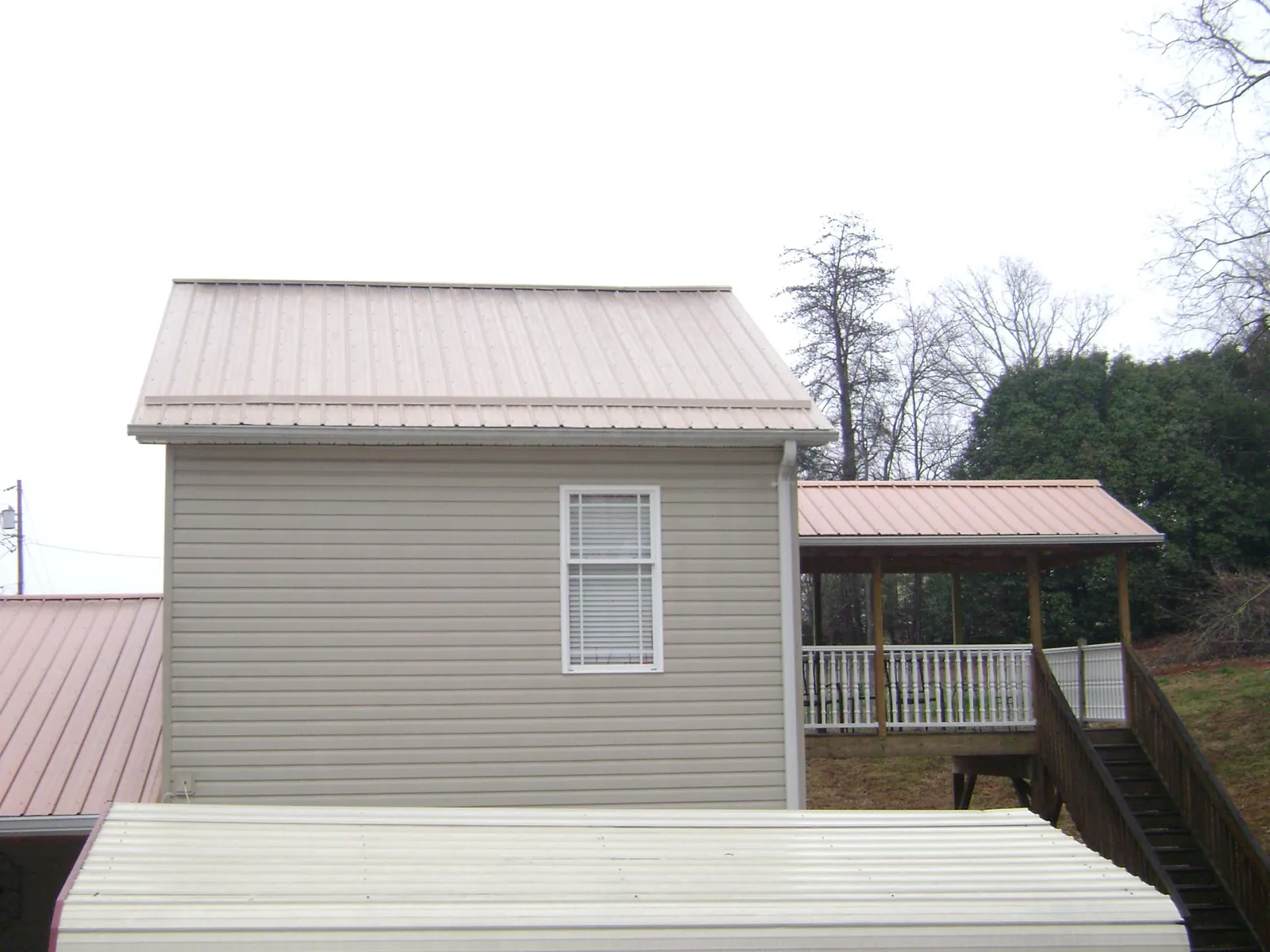 Tan metal roofs on a two story addition and attached porch, from a Roof Replacement job in Litchfield